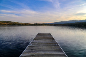 A wooden boat dock on a calm lake surrounded by pine trees. The Cove of Cascadia