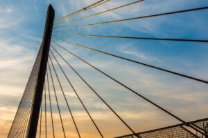 An upward view of the hanger cables on a metal bridge with a blue sky and wispy, cirrus clouds in the background. Creekside Health and Rehabilitation of Cascadia