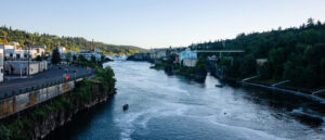 The waters of the Willamette River with a four-lane road on the left side and a dense foliage hill on the right.