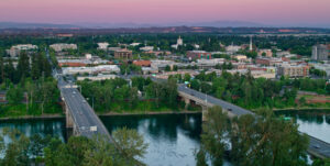 A summer sunset aerial shot two concrete bridges with cars crossing them that span a calm river with city buildings in the background.