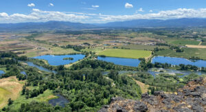 An aerial view of flat farm land with a winding river and three large ponds amongst the fields.